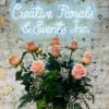 Pink roses arranged before a white floral wall with a glowing sign