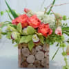 Coral roses and green orchids in a square wood vase
