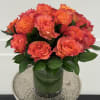 Orange roses arranged in a glass vase with dark green foliage