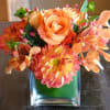 Orange floral arrangement in a square glass vase
