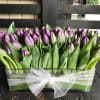 Purple tulips arranged in a clear rectangular vase with a white tulle bow