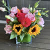 Mixed bouquet of pink, yellow, and red flowers in a square glass vase