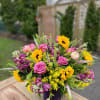 Mixed bouquet of pink roses, yellow sunflowers, and purple flowers in a purple vase