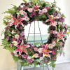 Circular floral wreath with pink lilies and purple blooms on a stand