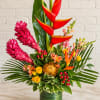 Tropical flower arrangement with red heliconia and pink ginger in a green vase.