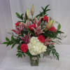 Pink lilies and red carnations in a glass vase with white hydrangea