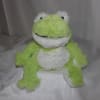 Green and white plush frog toy sitting on a bed