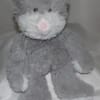 Gray plush teddy bear with a pink nose sitting on a bed