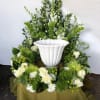 White urn surrounded by green and white floral arrangement