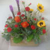 Mixed bouquet with orange roses, red carnations, and yellow sunflowers in a wooden box