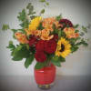 Mixed bouquet of red roses, sunflowers, and peach alstroemeria in a glass vase
