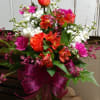 Mixed bouquet of red, orange, white, and pink flowers in a glass vase with a magenta ribbon