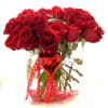 Red roses in a clear glass vase with a red heart ornament and ribbon