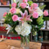 Vase arrangement of pink roses, white hydrangeas, and pink lilies in a clear glass cylinder