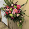 Standing floral spray with pink and burgundy blooms on a black easel