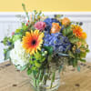 Mixed bouquet in a clear glass vase with blue hydrangeas, roses, and orange gerbera daisies