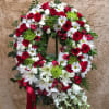 Circular wreath of red roses, white daisies, and lilies with a red ribbon
