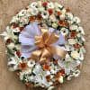 Round floral wreath with white lilies, daisies, and orange blooms on an easel
