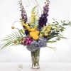 Tall mixed arrangement with blue hydrangeas, yellow roses, snapdragons, orchids, and calla lilies in a glass vase.