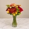 Bouquet of red roses and yellow-orange daisies in a clear glass vase