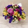 Mixed bouquet of purple, pink, and yellow flowers in a white vase