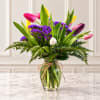 Colorful tulips and purple filler flowers in a glass vase with a twine bow