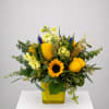 Yellow roses and a sunflower in a yellow vase with mixed greenery