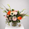 Mixed bouquet of orange, pink, and white flowers in a clear glass vase