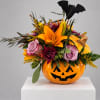 Halloween floral arrangement in a jack-o'-lantern container with roses and lilies