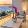 Potted pink orchid on a table beside a chair overlooking the ocean