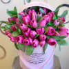 Pink tulips arranged in a round pink hatbox with green leaves