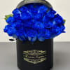 Round hatbox of vivid blue roses in a black cylinder container with gold script.