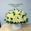 Large round hatbox of creamy white roses with dark green accents on a wooden table