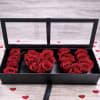 Red roses arranged in a black rectangular box with clear lid, surrounded by small red heart accents