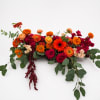 Long low arrangement of orange, red, and pink flowers with trailing greenery