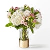 White hydrangea and pale pink rose bouquet in a clear glass vase with a gold base