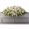 White floral casket spray with green accents on a gray casket