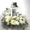 White floral arrangement around a white lantern with a candle inside
