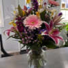 Stargazer Lilies, Iris, and Gerbera Daisy highlight this arrangement. ( Container may