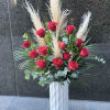Tall arrangement of red roses with pampas grass in a white vase
