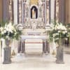 Large white floral altar arrangements flank a church altar with candles and a statue.