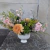 Pastel floral arrangement in a white pedestal vase with peach and pink blooms