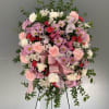 Pink and white floral wreath on a stand with a satin ribbon