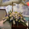 Large funeral flower arrangement with white and purple blooms beneath a crucifix