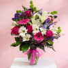 Mixed bouquet of pink roses, white lilies, and daisies in a glass vase