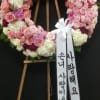 Pink and white floral wreath on a wooden stand with ribbon streamers