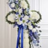Standing floral cross with white flowers, blue accents, and a blue ribbon