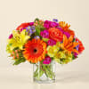 Bright mixed bouquet in a clear glass vase with orange, pink, yellow, and purple blooms