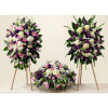 Three floral funeral arrangements in pink, purple, and white on stands and a low base