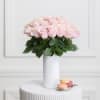Pink roses arranged in a white vase with macarons beside it